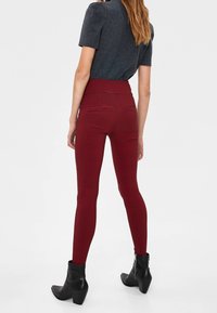 Rödrutiga leggings med hög midja, kombinerade med en mörk åtsittande topp och svarta ankelstövlar, som visar en smal siluett bakifrån.