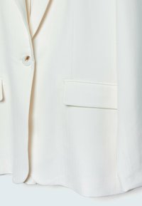 Bílý tailored blejzr vyrobený z hladké látky, s jedním knoflíkem na zapínání, klopovými límci a dvěma předními kapsami s plochými okraji.