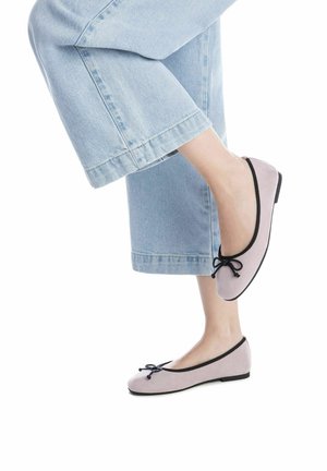 Bailarinas de ante rosa claro con ribete negro y detalle de lazo, combinadas con unos jeans de denim cortos. Los zapatos presentan un perfil bajo y una suela flexible.