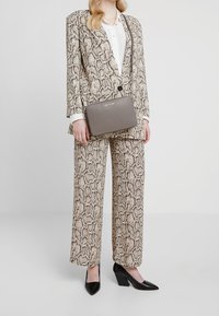 Traje con estampado de piel de serpiente en beige y marrón, con pantalones de pierna ancha y una chaqueta entallada. Acompañado de un bolso metálico gris y tacones negros.
