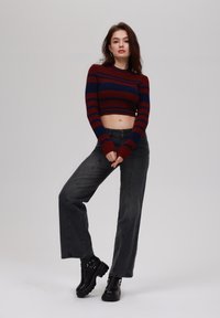 Red and navy striped cropped sweater, high-waisted black jeans, and black ankle boots with hardware accents, set against a neutral background.