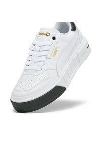 Fehér sneaker sima bőrből készült felsőrésszel, perforált orral és fekete gumitalppal. Arany logó részletekkel és lapos fehér fűzőkkel rendelkezik.