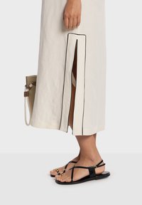 Robe midi en lin blanc cassé avec des bordures noires, fente latérale ; associée à des sandales plates noires avec des perles dorées en accent.