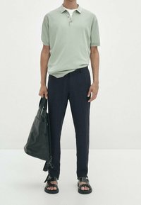 Hellgrünes, gemustertes Poloshirt, marineblaue tapered Hose, schwarze Lederhandtasche und schwarze Sandalen mit verstellbaren Riemen. Minimalistisches Design.
