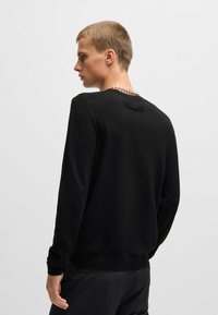 Felpa nera a maniche lunghe realizzata in tessuto morbido, con collo rotondo e polsini a coste. Design minimalista con un'etichetta di marca sulla parte posteriore.