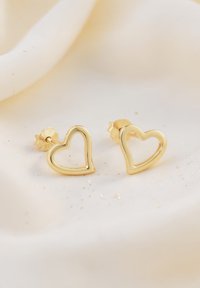 Orecchini a bottone a forma di cuore in oro con un design vuoto, caratterizzati da bordi lisci e un retro testurizzato. Brillano con punti luminosi sullo sfondo.