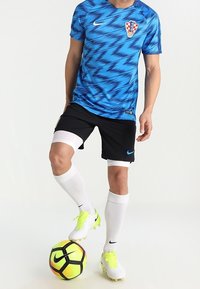 Equipación de fútbol azul y negra con un patrón en zigzag, medias blancas y zapatillas amarillas brillantes. La camiseta tiene un escudo del equipo en el pecho.