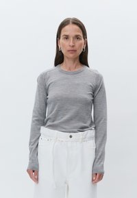 Haut en maille gris à manches longues avec un col rond et des poignets côtelés, associé à un pantalon blanc taille haute avec une taille à cordon.