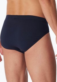 Dunkelblaue Baumwoll-Schwimmslips mit glatter Textur und niedrigem Schnitt, ausgestattet mit gestickten Nähten und einem minimalistischen Design.