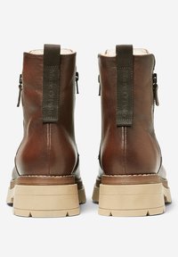 Botas de cuero marrón hasta el tobillo con un acabado suave, que presentan una suela gruesa beige, cremalleras laterales y tiradores de tela.