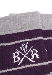 Lila och grå randiga strumpor med en mjuk textur; har ett vitt emblem med korsade element och bokstäverna "B", "R" i designen.
