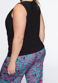 Svart ärmlös topp med en avslappnad passform, i kombination med livfulla byxor i turkos och rosa tigerstrimmigt mönster.