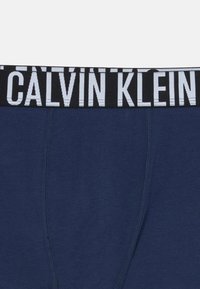 Mutande in cotone blu navy con una ampia fascia nera caratterizzata dalla scritta "CALVIN KLEIN" stampata in bianco. Texture liscia con una forma aderente.