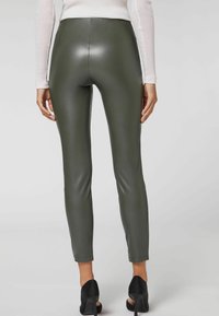 Neplederen leggings in donkergroen, met een aansluitend ontwerp en een elegante textuur. Gemaakt in combinatie met zwarte open-taille hakken. Achteraanzicht weergegeven.