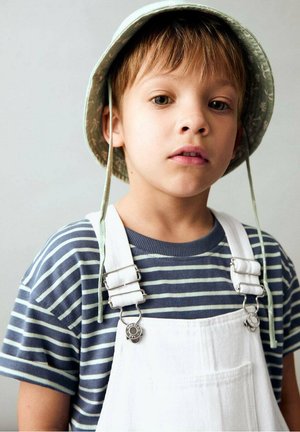 Gestreiftes kurzärmliges Hemd in Marineblau und Hellblau, mit weißen verstellbaren Latzhosen mit metallischen Clips und einem hellgrünen Bucket Hat.