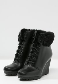 Bottines compensées noires en cuir, dotées d'un col en fausse fourrure, de lacets avec œillets, et de semelles texturées pour l'adhérence.