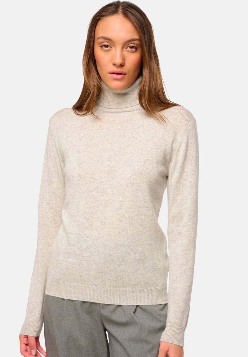 Un pull à col roulé gris clair fabriqué à partir d'un tissu doux et texturé, avec des manches longues et des poignets côtelés, associé à un pantalon gris sur mesure.