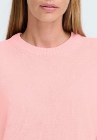 Rosa stickad tröja med en ribbad rund halsringning och en mjuk yta, med fokus på kroppsområdet och detaljerna vid halsringningen.