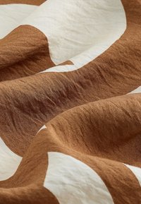 Lininė medžiaga su banguota tekstūra pasižymi dideliais, netaisyklingais rudos ir baltos spalvos raštais. Paviršius atrodo minkštas ir šiek tiek raukšlėtas.