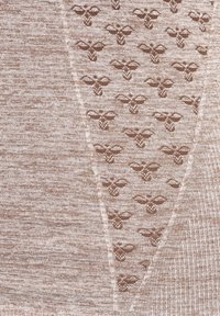 Beige neulekangas, jossa on hienovarainen rakenne pienillä ruskeilla kukkakuviolla. Pehmeä pinta, jossa on röyhelömäinen ulkonäkö ja sileä viimeistely.