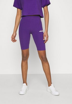 Violetit pyöräilyshortsit mukavalla istuvuudella, etuosassa logo ja sileä pinta, yhdistettyinä valkoisiin lenkkarit.