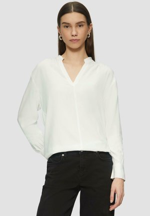 White long-sleeve blouse with a V-neck, made of smooth fabric. Features relaxed fit and subtle gathering at cuffs. Paired with black pants.