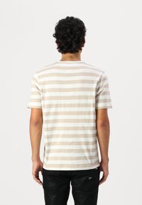 Beige and white striped short-sleeve t-shirt made of cotton, with a round neckline and a regular fit, worn with black pants.