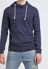 Sweat-shirt à capuche bleu marine avec un motif à rayures texturées, doté d'une fermeture à cordon de serrage et de poches kangourou à l'avant. Tissu doux.