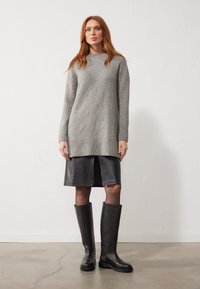 Suéter de punto gris con dobladillo acanalado, falda de cuero negra con una abertura frontal y botas de cuero negras hasta la rodilla con suela gruesa.