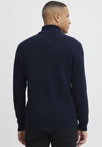 Pulover tricotat de culoare albastru marin cu un model texturat, guler înălțat și mâneci și tiv cu nervuri. Vedere din spate care arată un design strâns.