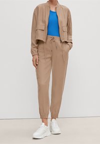 Beige cropped bomberjakke med to forlommer, parret med beige joggers med elastisk talje, og hvide chunky sneakers. Lys blå top under.