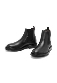 Bottes Chelsea en cuir noir avec panneaux latéraux élastiques, bout arrondi, languette de maintien et détails texturés à l'arrière. Semelle plate en caoutchouc.