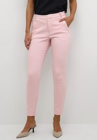 Pink tailored trousers with a slim fit, high waist, side pockets, and a smooth, stretchy fabric. Worn with beige pointed heels.