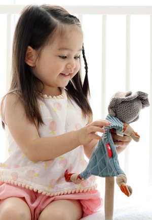 Young girl smiling while holding and playing with a soft stuffed monkey toy wearing a blue outfit.