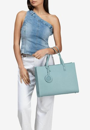 Borsa tote in pelle azzurro chiaro con superficie testurizzata, due manici e un ciondolo circolare. Il design è rettangolare con un'estetica minimalista.