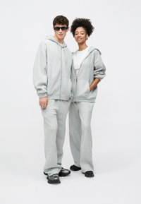 Pilki gobtavai megztiniai su gobtuvu ir treningai iš minkštos medžiagos, turintys kišenes kengūros stiliaus, laisvo kirpimo ir kontrastingas baltas siūles. Avimi juodi sportbačiai.