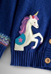 Stickad blå cardigan med en vit enhörningspatch med rosa man, grön sköld och stjärna, samt träknappar och ribbad textur.