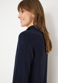 Maglione pullover blu navy con collo a costine e design a trecce sulle maniche, caratterizzato da una superficie liscia e una silhouette aderente.