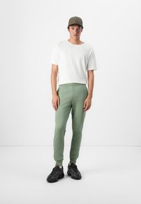 Grønne sweatpants med elastisk talje, parret med en enkel hvid T-shirt med korte ærmer og en ternet kasket, båret med sorte sportssko.