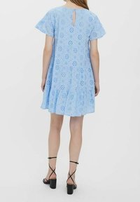 Robe bleu clair à étages avec manches courtes à volants, broderie florale, ouverture en trou de serrure dans le dos, portée avec des sandales à talons blocs.