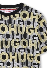 Maglietta nera con logo "HUGO" ripetuto in giallo e grigio, caratterizzata da una tipografia audace. Collo rotondo e maniche corte. Materiale in cotone.