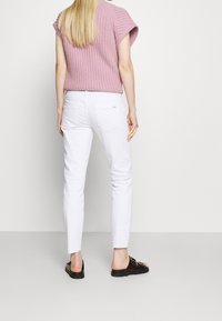 Un haut tricoté rose clair à manches courtes porté sur un jean blanc slim-fit ; le pantalon blanc présente un ourlet effiloché et des détails de poche arrière. Des chaussures noires à enfiler.