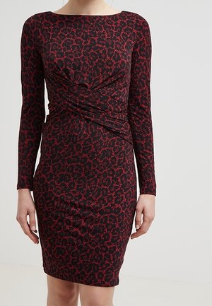 Frau trägt ein eng anliegendes schwarzes Kleid mit rotem Leopardenmuster, langen Ärmeln und einem gedrehten Detail an der Taille.
