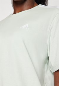 T-shirt en coton vert clair à manches courtes, avec un petit logo Adidas blanc sur la poitrine et une texture lisse.