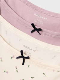 Set med tre t-shirts i bomull: en ljusrosa, en krämfärgad med blommönster och en ljusrosa, var och en med en dekorativ svart rosett vid halsen.