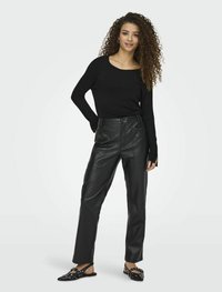 Maglietta nera a maniche lunghe abbinata a pantaloni finti in pelle nera a vita alta e strutturati. Le scarpe hanno un design piatto con accentuazioni a borchie bianche.