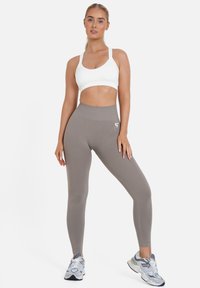 Sujetador deportivo blanco y leggings en tono topo con una cinturilla alta, que presentan un tejido texturizado y un pequeño logo en la pierna izquierda.