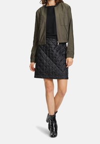 Olivgrön bomberjacka med ribbat mönster, kombinerad med en svart vadderad minikjol och glänsande svarta ankelstövlar.