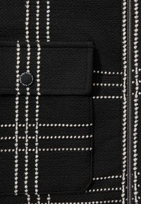 Black textile with white grid pattern, featuring a zip closure and a pocket with a circular button. Textured surface adds depth.