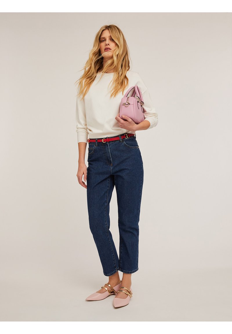 Blusa blanca de manga larga, cinturón rojo, vaqueros de tiro alto azules, bailarinas rosas con acentos dorados y un pequeño bolso rosa.